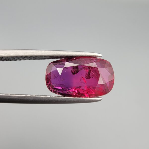 A premium 4.02-carat natural Mozambique ruby gemstone held horizontally by jeweler's tweezers, showcasing an elegant elongated cushion cut, vibrant purplish-red body color, and stunning transparent clarity with distinct internal crystal inclusions.