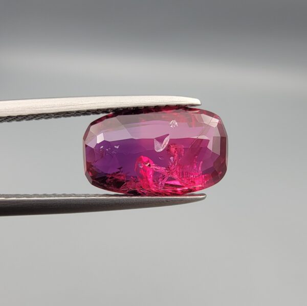 A premium 4.02-carat natural Mozambique ruby gemstone held horizontally by jeweler's tweezers, showcasing an elegant elongated cushion cut, vibrant purplish-red body color, and stunning transparent clarity with distinct internal crystal inclusions.