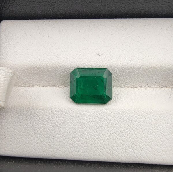 ​A premium 2.98-carat natural Zambian emerald gemstone displaying an elegant octagonal step cut with sharp parallel facet lines and a rich green transparency, resting inside a textured white leather jewelry box liner.