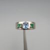 ​A premium handcrafted men's 925 sterling silver ring featuring a large oval-cut natural Ceylon blue sapphire center stone flanked by two vibrant, square-cut Swat Valley emerald side stones, displayed on a clean reflective surface.