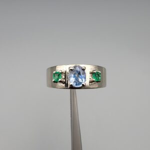 ​A premium handcrafted men's 925 sterling silver ring featuring a large oval-cut natural Ceylon blue sapphire center stone flanked by two vibrant, square-cut Swat Valley emerald side stones, displayed on a clean reflective surface.