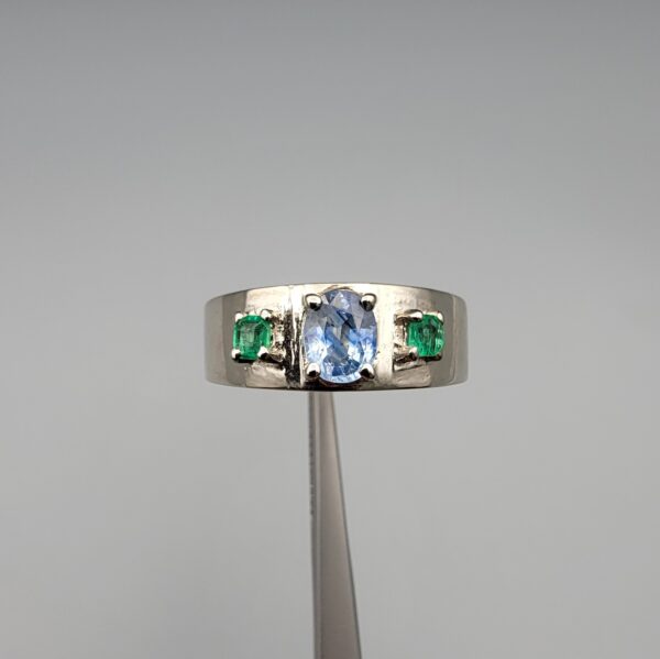​A premium handcrafted men's 925 sterling silver ring featuring a large oval-cut natural Ceylon blue sapphire center stone flanked by two vibrant, square-cut Swat Valley emerald side stones, displayed on a clean reflective surface.