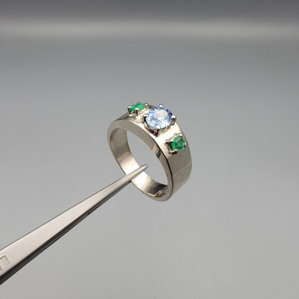​A premium handcrafted men's 925 sterling silver ring featuring a large oval-cut natural Ceylon blue sapphire center stone flanked by two vibrant, square-cut Swat Valley emerald side stones, displayed on a clean reflective surface.
