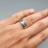 ​A premium handcrafted men's 925 sterling silver ring featuring a large oval-cut natural Ceylon blue sapphire center stone flanked by two vibrant, square-cut Swat Valley emerald side stones, displayed on a clean reflective surface.