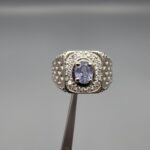 ​A premium men's 925 sterling silver statement ring featuring an oval-cut natural Ceylon blue sapphire centerpiece surrounded by a brilliant double border of sparkling white zircons, displayed from multiple professional angles on a reflective surface.