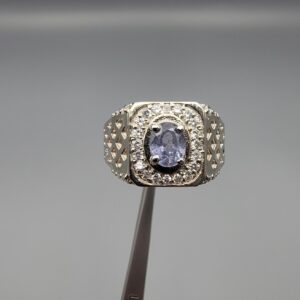 ​A premium men's 925 sterling silver statement ring featuring an oval-cut natural Ceylon blue sapphire centerpiece surrounded by a brilliant double border of sparkling white zircons, displayed from multiple professional angles on a reflective surface.