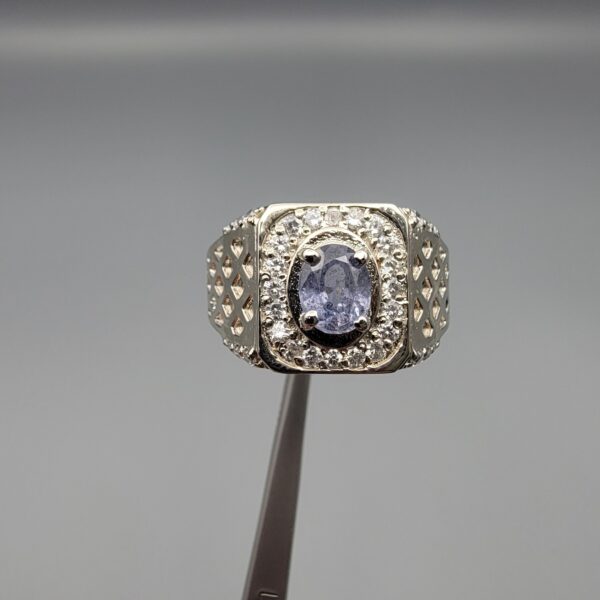 ​A premium men's 925 sterling silver statement ring featuring an oval-cut natural Ceylon blue sapphire centerpiece surrounded by a brilliant double border of sparkling white zircons, displayed from multiple professional angles on a reflective surface.