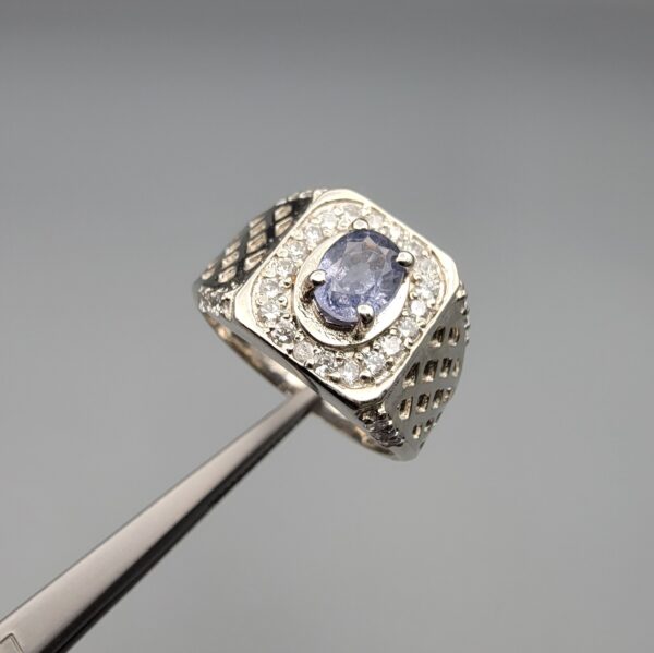 ​A premium men's 925 sterling silver statement ring featuring an oval-cut natural Ceylon blue sapphire centerpiece surrounded by a brilliant double border of sparkling white zircons, displayed from multiple professional angles on a reflective surface.