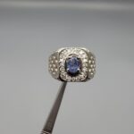 ​A premium men's 925 sterling silver statement ring featuring an oval-cut natural Ceylon blue sapphire centerpiece surrounded by a brilliant double border of sparkling white zircons, displayed from multiple professional angles on a reflective surface.