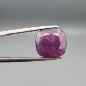 ​A massive 9.65-carat natural, unheated Ceylon purple sapphire (Khooni Neelam) showing a premium faceted cushion mixed cut, displaying a rich purple body color with mysterious undertones, resting inside a textured white leather jewelry box liner.