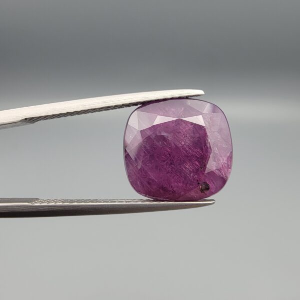 ​A massive 9.65-carat natural, unheated Ceylon purple sapphire (Khooni Neelam) showing a premium faceted cushion mixed cut, displaying a rich purple body color with mysterious undertones, resting inside a textured white leather jewelry box liner.