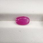 ​A premium 2.61-carat natural, unheated Afghan ruby from Kabul (Jegdalek) with a faceted oval cut, displaying a vibrant pinkish-red translucent color profile held securely in professional jeweler's tweezers.