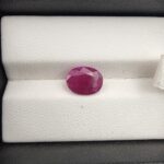 A premium 2.97-carat natural, unheated Mozambican ruby showing a faceted oval cut with a rich translucent red body color, held securely in professional jeweler's tweezers.