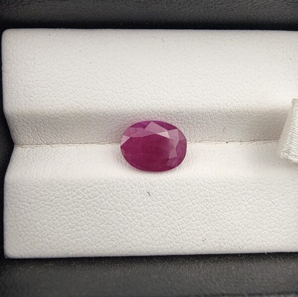 A premium 2.97-carat natural, unheated Mozambican ruby showing a faceted oval cut with a rich translucent red body color, held securely in professional jeweler's tweezers.