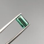 A natural 2.11-carat greenish-blue tourmaline from Africa, featuring a premium faceted rectangle emerald cut with excellent transparency and parallel facet lines, held in professional jeweler's tweezers.