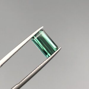 A natural 2.11-carat greenish-blue tourmaline from Africa, featuring a premium faceted rectangle emerald cut with excellent transparency and parallel facet lines, held in professional jeweler's tweezers.