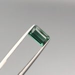 A natural 2.63-carat greenish-blue tourmaline from Africa, displaying a premium faceted rectangle emerald cut with deep color saturation and flawless transparency, held firmly in professional jeweler's tweezers.