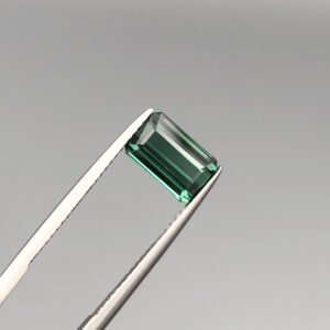 A natural 2.63-carat greenish-blue tourmaline from Africa, displaying a premium faceted rectangle emerald cut with deep color saturation and flawless transparency, held firmly in professional jeweler's tweezers.