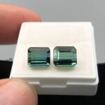 A perfectly matched pair of natural greenish-blue African tourmalines totaling 4.63 carats, featuring step-cut rectangle silhouettes with excellent transparency, resting side by side in a white collector's gem box.