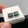 A perfectly matched pair of natural greenish-blue African tourmalines totaling 4.63 carats, featuring step-cut rectangle silhouettes with excellent transparency, resting side by side in a white collector's gem box.