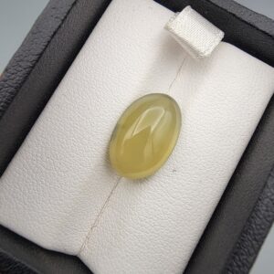 ​A rare 7.59-carat natural Italian Vesuvianite cabochon held securely in gemstone tweezers. The stone exhibits a smooth, high-dome oval cut with excellent symmetry, showcasing a rich, uniform chartreuse-green to olive-green hue with a bright, glassy surface luster.