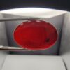 ​A massive 22.20-carat oval natural Yemeni carnelian agate cabochon held in tweezers. Without direct light, the gemstone displays an opaque, deep liver-brown tone, but under direct backlighting, it transforms into a fully translucent, deep crimson-red stone showing faint internal agate structure.