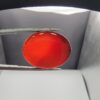 ​A massive 22.07-carat oval natural Yemeni carnelian agate cabochon held securely in tweezers. In normal lighting, the stone shows a smooth, glossy, deep liver-brown body, but under strong direct backlighting, it glows with a rich, uniform translucent reddish-crimson color.