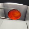 ​A premium 19.17-carat natural oval Yemeni carnelian agate cabochon held in tweezers. While appearing dark brown in flat shadow, strong backlighting transforms it into a brilliant, translucent fiery orange gemstone displaying elegant, natural curved agate zoning lines.