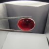 A massive 21.58-carat oval natural Yemeni carnelian agate cabochon held securely in tweezers. In normal lighting as seen in input_file_0.png, the stone shows a smooth, glossy, deep liver-brown body. Under strong direct backlighting in input_file_1.png and input_file_2.png, it glows with a rich, uniform translucent reddish-crimson color, revealing elegant natural parallel banding lines along its lower edge.