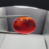 A premium 16.65-carat natural oval Yemeni carnelian agate cabochon held in tweezers. While appearing dark brown with a dense core in flat ambient lighting, strong backlighting transforms it into a brilliant, translucent fiery orange gemstone displaying elegant, natural curved agate zoning lines and parallel waterline patterns across its face.