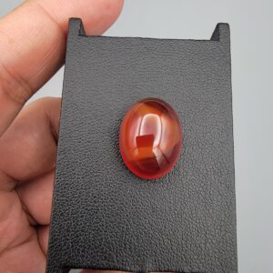 ​A heavy 16.43-carat natural oval carnelian agate cabochon from Yemen, displaying a rich, deep translucent reddish-orange body color with distinct internal zoning lines characteristic of authentic Yemeni Aqeeq.