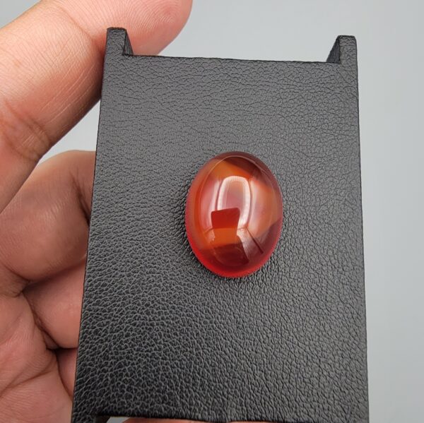 ​A heavy 16.43-carat natural oval carnelian agate cabochon from Yemen, displaying a rich, deep translucent reddish-orange body color with distinct internal zoning lines characteristic of authentic Yemeni Aqeeq.