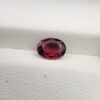​A premium 1.15-carat natural Mozambique Rubellite Tourmaline gemstone resting flat on a white textured leather insert inside a display box. The loose oval faceted gemstone showcases an exceptionally rich, deep crimson and magenta-red body color with crisp, light-reflecting crown facets.