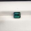 ​A premium 2.35-carat natural African Greenish-Blue Tourmaline gemstone shown across two views. In the first image, the stone is held securely in silver metal tweezers against a clean gray background, flashing intense teal-blue and minty sea-green light from its crisp pavilion facets. The second image shows the loose octagon-cut gemstone resting flat on a white textured display insert inside a black box, highlighting its rich, deep blue-green body color.