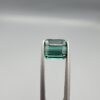 ​A premium 2.29-carat natural African Greenish-Blue Tourmaline gemstone shown across two views. In the first image, the stone is held securely in silver metal tweezers against a clean gray background, flashing intense teal-blue and minty sea-green light from its crisp pavilion facets. The second image shows the loose octagon-cut gemstone resting flat on a white textured display insert inside a black box, highlighting its rich, deep blue-green body color.