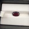 ​A premium 3.60-carat natural Madagascar Red Garnet gemstone shown across three product views. The stone is photographed held securely in silver metal tweezers against a clean gray background and resting on a white textured display insert inside a black box, showcasing its rich crimson-red body color and vibrant, fire-red sparkling facets.