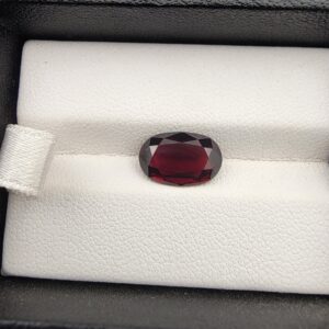 A premium 3.60-carat natural Madagascar Red Garnet gemstone shown across three product views. The stone is photographed held securely in silver metal tweezers against a clean gray background and resting on a white textured display insert inside a black box, showcasing its rich crimson-red body color and vibrant, fire-red sparkling facets.
