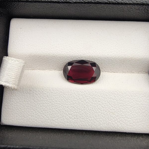 ​A premium 3.60-carat natural Madagascar Red Garnet gemstone shown across three product views. The stone is photographed held securely in silver metal tweezers against a clean gray background and resting on a white textured display insert inside a black box, showcasing its rich crimson-red body color and vibrant, fire-red sparkling facets.