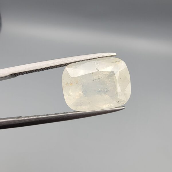 Official Galaxy Gemological Institute (GGI) Gemstone Report for a 7.18-carat Natural Colorless Sapphire. The certificate lists report number KHI260619001 and displays a digital product image of the loose, cushion-cut semi-transparent stone resting on a white reflective surface, emphasizing its clear, white icy tone and prominent step-and-mixed faceting architecture.