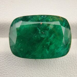 ​A rare, heavyweight 13.67-carat natural Pakistani Emerald gemstone resting flat on a white textured presentation insert inside a display box. The loose, earth-mined beryl gem is precision cut into a classic, well-proportioned cushion shape, displaying an incredibly deep, rich grass-green body color with classic velvety undertones.