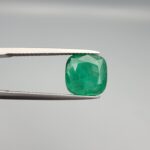 ​A premium 3.84-carat natural Pakistani Emerald gemstone resting flat on a white textured leather insert inside a display box. The loose, earth-mined beryl gem is precision cut into an elegant, well-proportioned cushion shape, exhibiting an incredibly rich, deep grass-green color with unique internal clouds and beautiful inclusion patterns that catch the light.