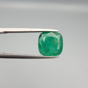 ​A premium 3.84-carat natural Pakistani Emerald gemstone resting flat on a white textured leather insert inside a display box. The loose, earth-mined beryl gem is precision cut into an elegant, well-proportioned cushion shape, exhibiting an incredibly rich, deep grass-green color with unique internal clouds and beautiful inclusion patterns that catch the light.