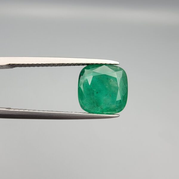 ​A premium 3.84-carat natural Pakistani Emerald gemstone resting flat on a white textured leather insert inside a display box. The loose, earth-mined beryl gem is precision cut into an elegant, well-proportioned cushion shape, exhibiting an incredibly rich, deep grass-green color with unique internal clouds and beautiful inclusion patterns that catch the light.