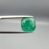 ​A premium 3.84-carat natural Pakistani Emerald gemstone resting flat on a white textured leather insert inside a display box. The loose, earth-mined beryl gem is precision cut into an elegant, well-proportioned cushion shape, exhibiting an incredibly rich, deep grass-green color with unique internal clouds and beautiful inclusion patterns that catch the light.