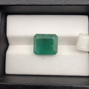 ​A premium, heavyweight 7.41-carat natural Zambian Emerald gemstone resting flat on a white textured presentation insert inside a display box. The loose, earth-mined beryl gem showcases a deeply saturated, vibrant grass-green body color with an excellent table spread and fine symmetry.
