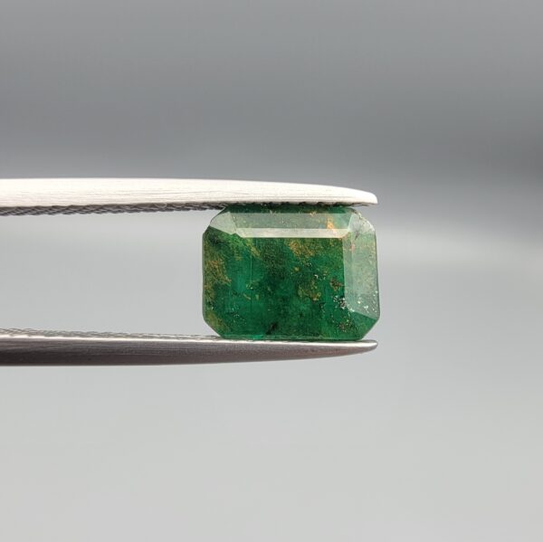 ​A rare 2.11-carat natural Swat Valley Emerald gemstone resting flat on a white textured leather insert inside a black presentation box. The loose beryl gemstone showcases an intensely vibrant green body color beautifully blended with warm, unique yellowish accents and shimmering crystalline pyrite inclusions trapped inside its core.