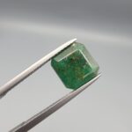 A premium 3.45-carat natural Swat Valley Emerald gemstone resting flat on a white textured leather insert inside a black presentation box. The loose beryl gemstone showcases an intensely vibrant green body color beautifully filled with warm yellowish accents, shimmering pyrite inclusions, and a distinct, natural white matrix inclusion in the upper corner that mimics a majestic snow-capped mountain landscape.