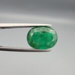 A premium 4.69-carat natural Pakistani Emerald gemstone resting flat on a white textured presentation insert inside a black display box. The loose, earth-mined beryl gem is precision cut into an elegant, well-proportioned oval shape, showcasing a deeply saturated, classic grass-green body color with an excellent face-up table spread.