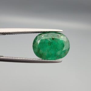A premium 4.69-carat natural Pakistani Emerald gemstone resting flat on a white textured presentation insert inside a black display box. The loose, earth-mined beryl gem is precision cut into an elegant, well-proportioned oval shape, showcasing a deeply saturated, classic grass-green body color with an excellent face-up table spread.