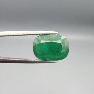 A premium 3.80-carat natural Swat Valley Emerald gemstone held securely in metal gemstone tweezers against a smooth gray studio background. The loose, earth-mined beryl gem is precision cut into an elegant cushion shape, displaying an intense, saturated alpine-green body color with beautifully layered internal growth features and fine facet symmetry.